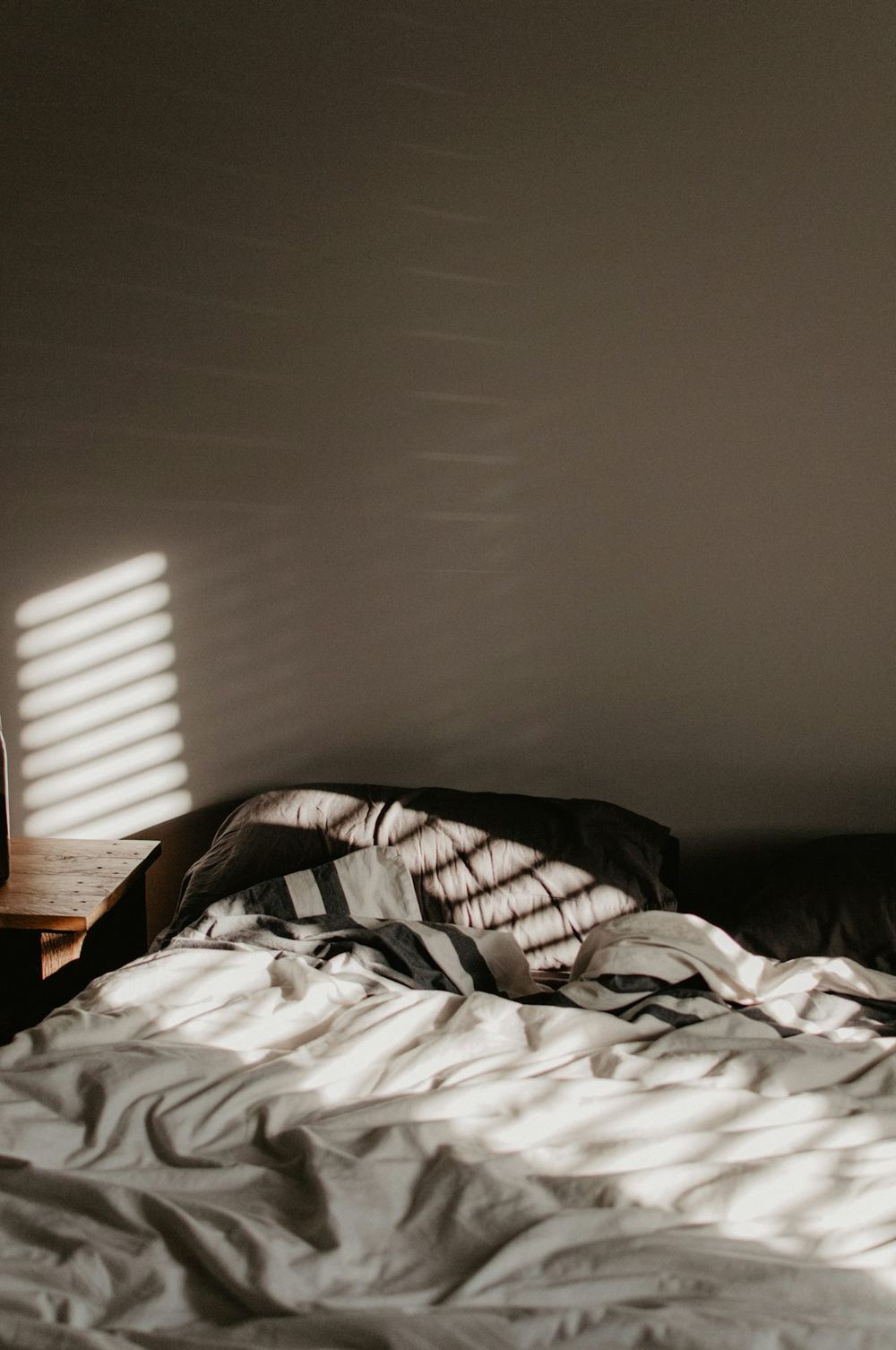 Cama deshecha con luz de mañana entre las lamas